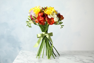 Photo of Bouquet of beautiful spring freesia flowers on table against color background