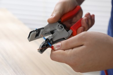 Photo of Professional electrician stripping wiring on blurred background, closeup