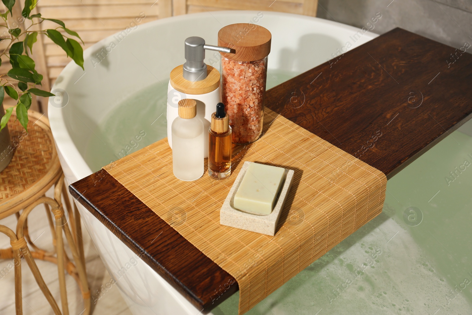 Photo of Wooden tray with spa products on bath tub in bathroom