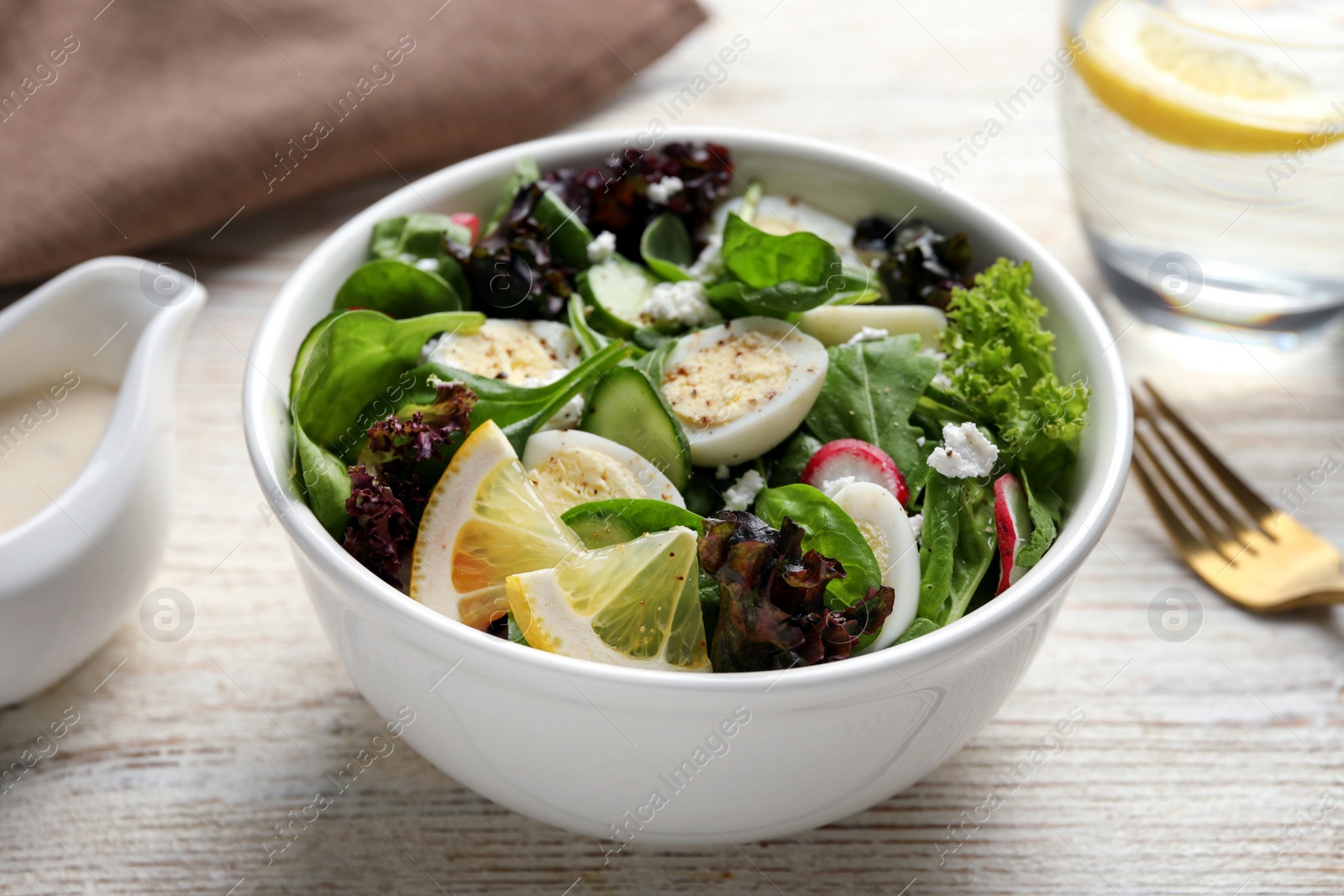 Photo of Delicious salad with boiled eggs, vegetables and lemon in bowl on white wooden table, closeup