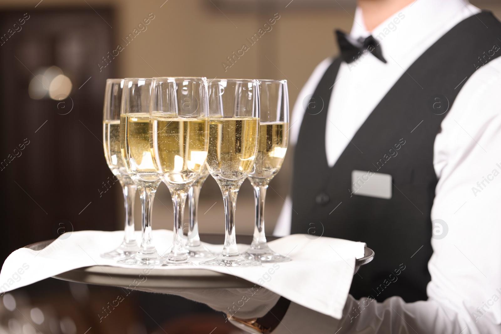 Photo of Butler holding tray with glasses of sparkling wine in restaurant, closeup