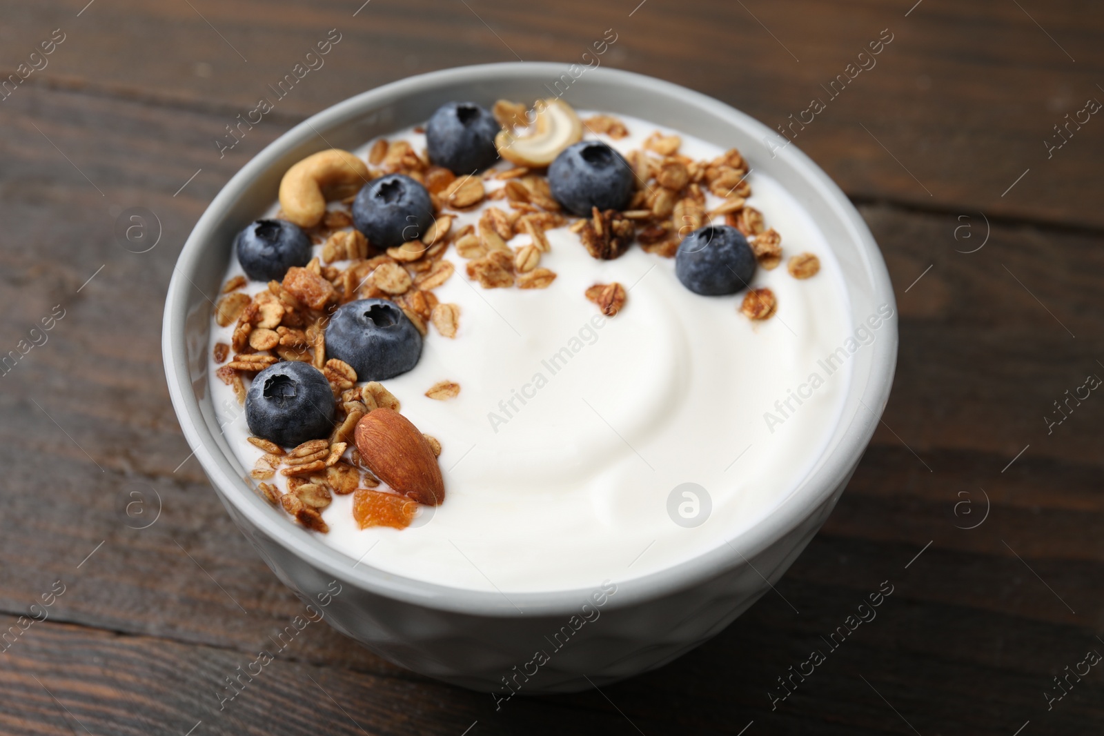 Photo of Bowl with yogurt, blueberries and granola on wooden table, closeup