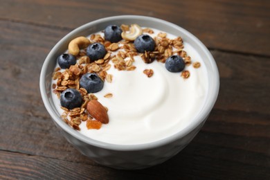 Bowl with yogurt, blueberries and granola on wooden table, closeup