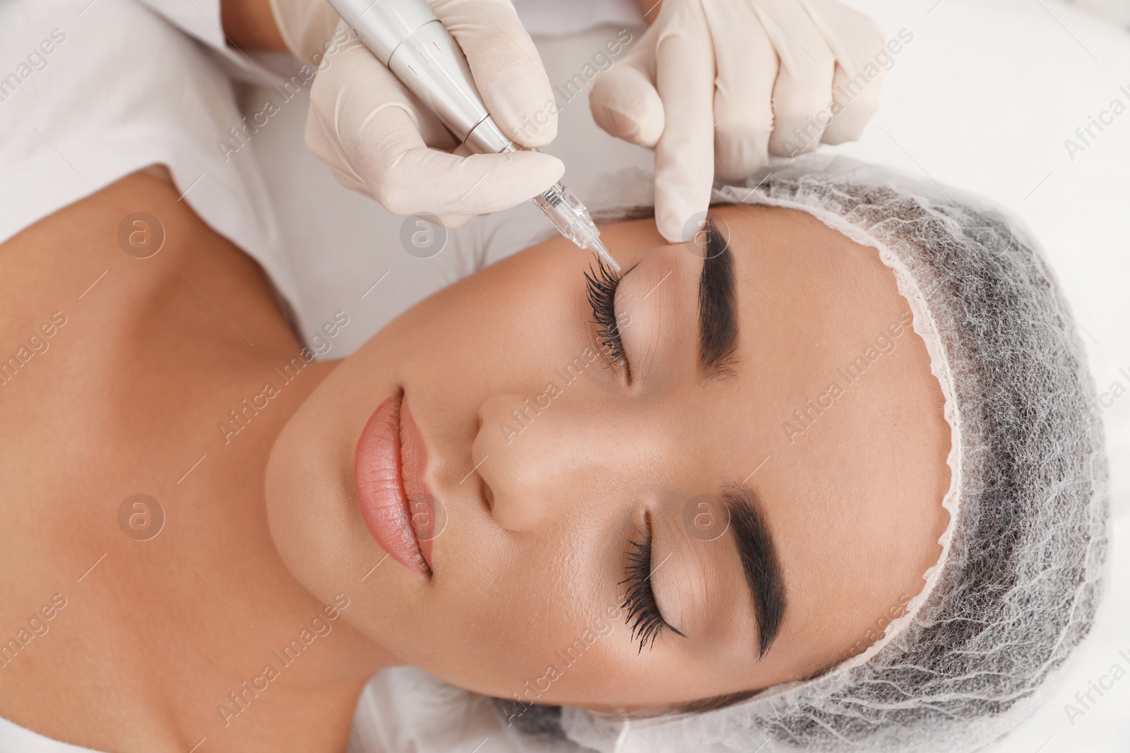 Photo of Young woman undergoing procedure of permanent eye makeup in tattoo salon