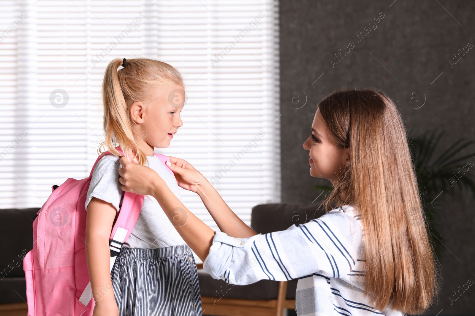 Photo of Young mother helping her little child to put on school bag at home