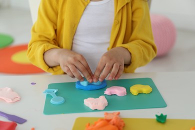 Photo of Little girl sculpting with play dough at table indoors, closeup