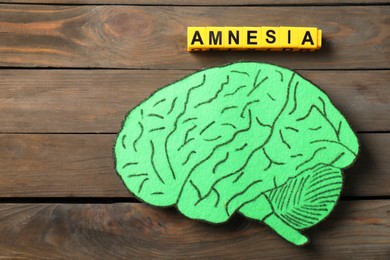 Photo of Yellow cubes with word Amnesia and paper cutout of human brain on wooden table, top view
