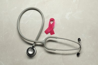 Photo of Pink ribbon and stethoscope on light grey table, flat lay. Breast cancer awareness