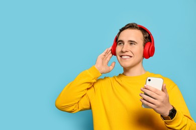 Photo of Handsome young man with headphones and modern smartphone on light blue background. Space for text