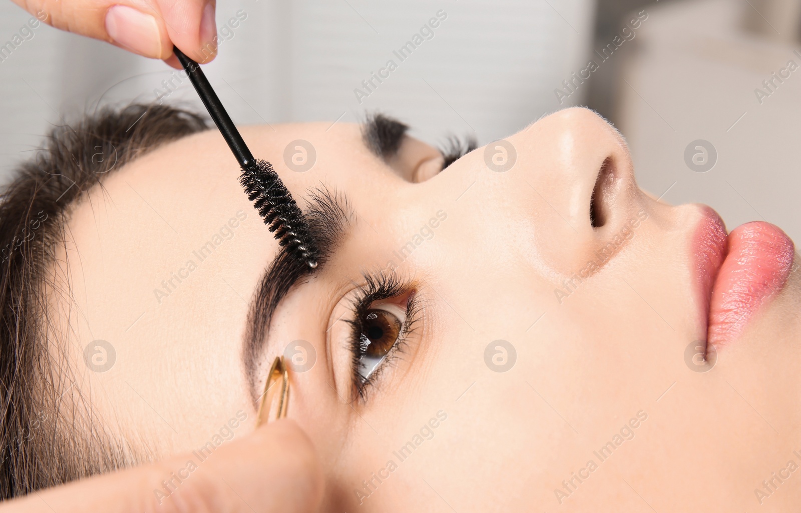Photo of Young woman having professional eyebrow correction procedure in beauty salon, closeup