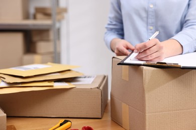 Photo of Parcel packing. Post office worker with clipboard writing notes at wooden table indoors, closeup