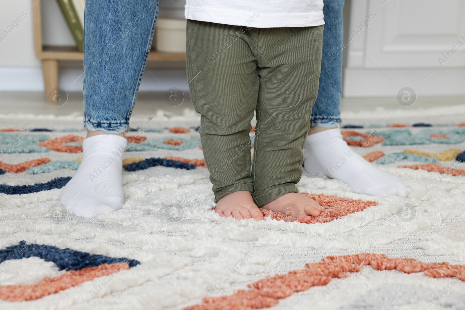 Photo of Mother supporting her son while he learning to walk on carpet indoors, closeup