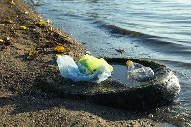 Photo of Plastic trash and tire on sand near water. Environment pollution