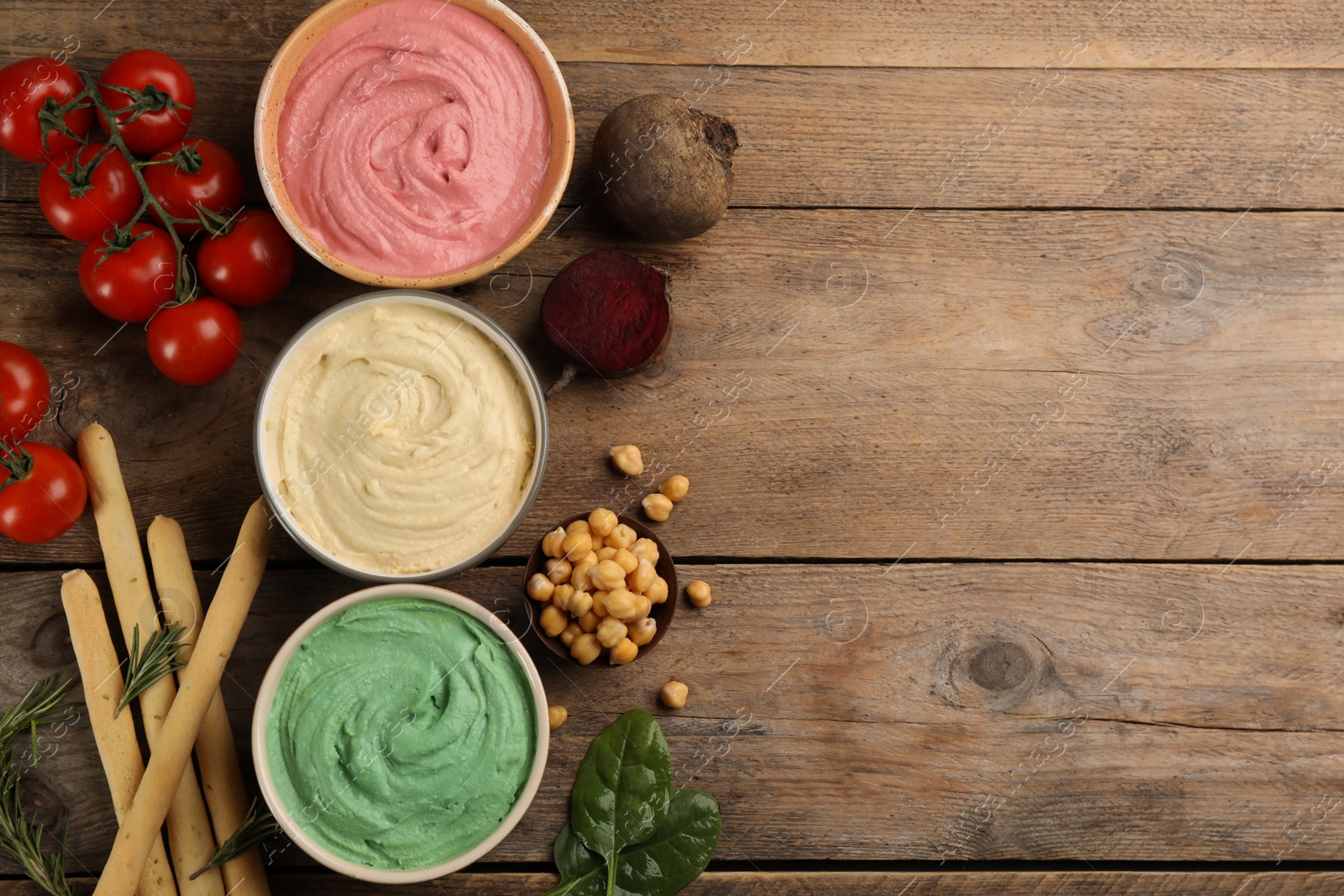 Photo of Different kinds of tasty hummus with bread sticks on wooden table, flat lay