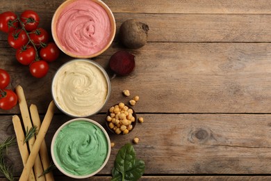 Photo of Different kinds of tasty hummus with bread sticks on wooden table, flat lay