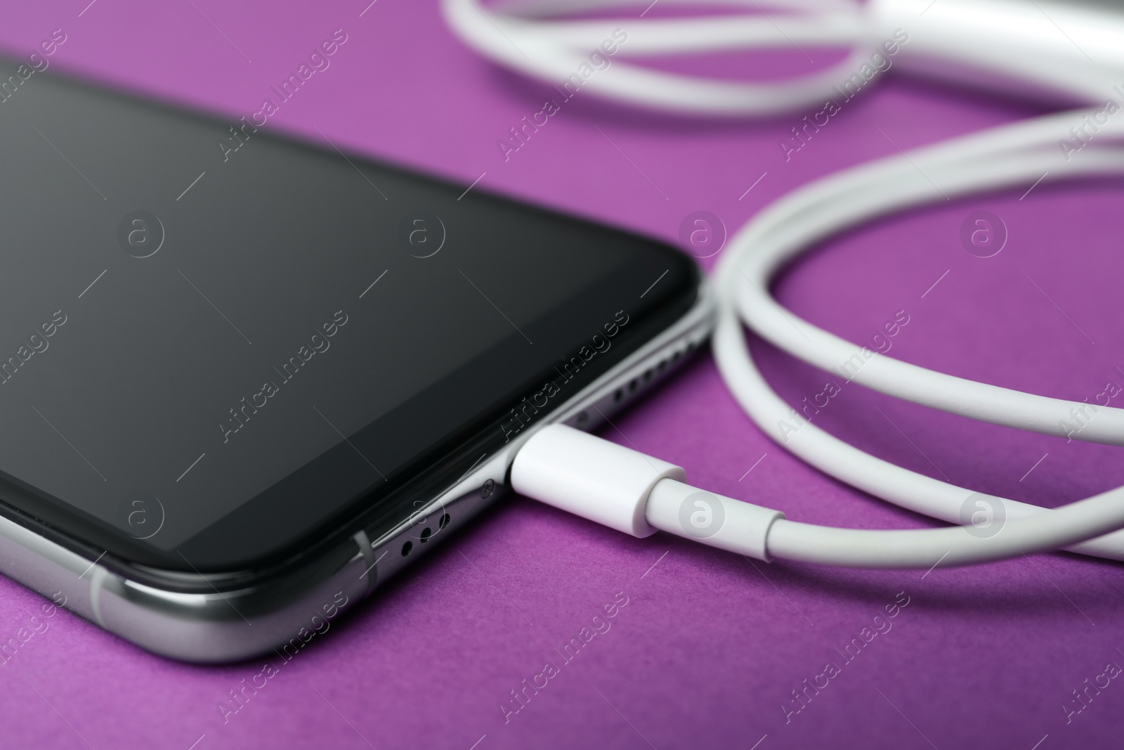 Photo of Smartphone and charge cable on purple background, closeup. Modern technology