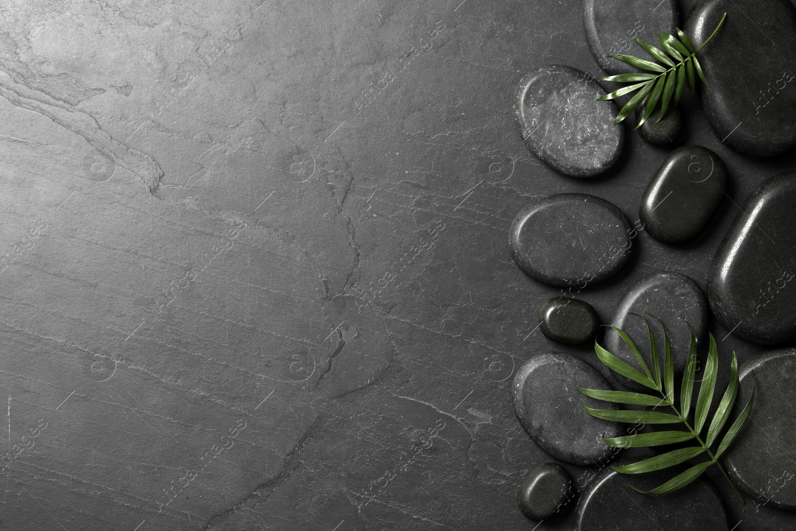 Photo of Spa stones and green leaves on black table. Space for text