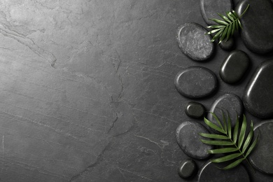 Photo of Spa stones and green leaves on black table. Space for text