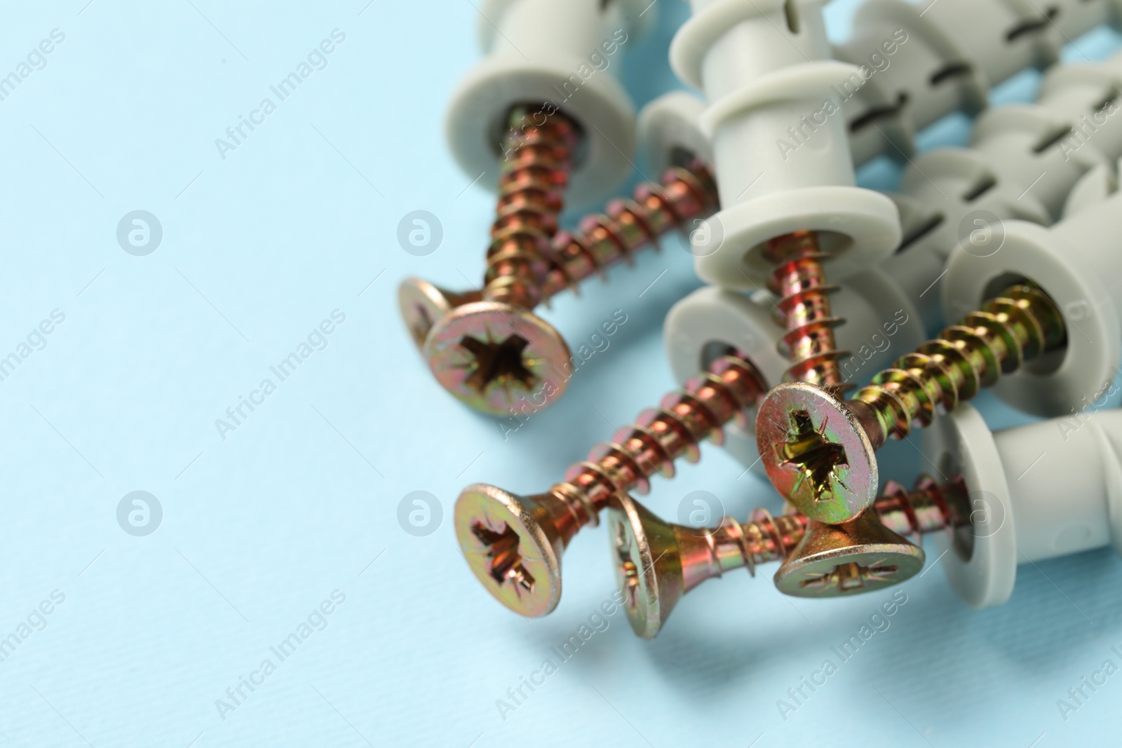 Photo of Many metal screws with dowels on light blue background, closeup. Space for text