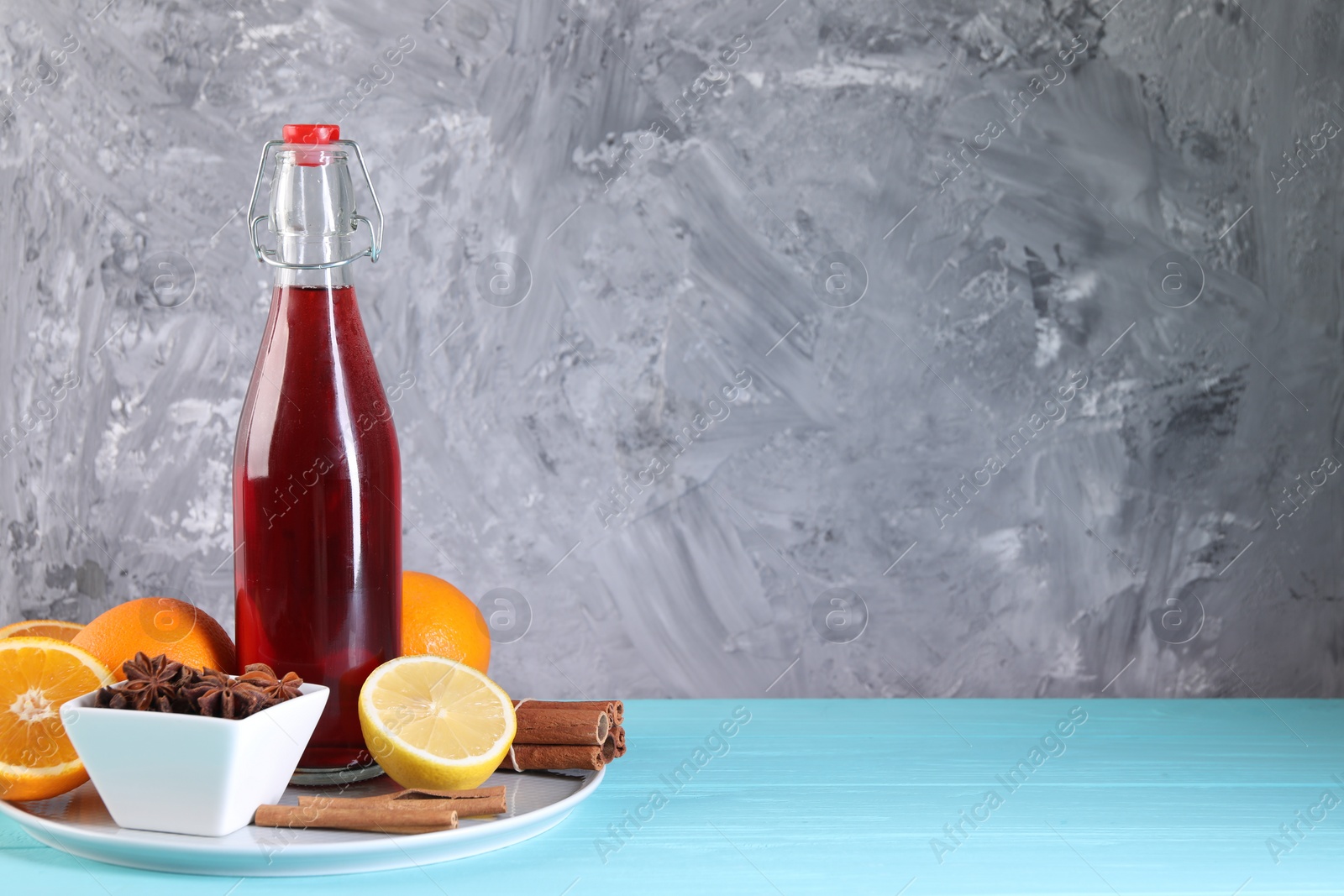 Photo of Bottle of aromatic punch drink and ingredients on light blue table, space for text