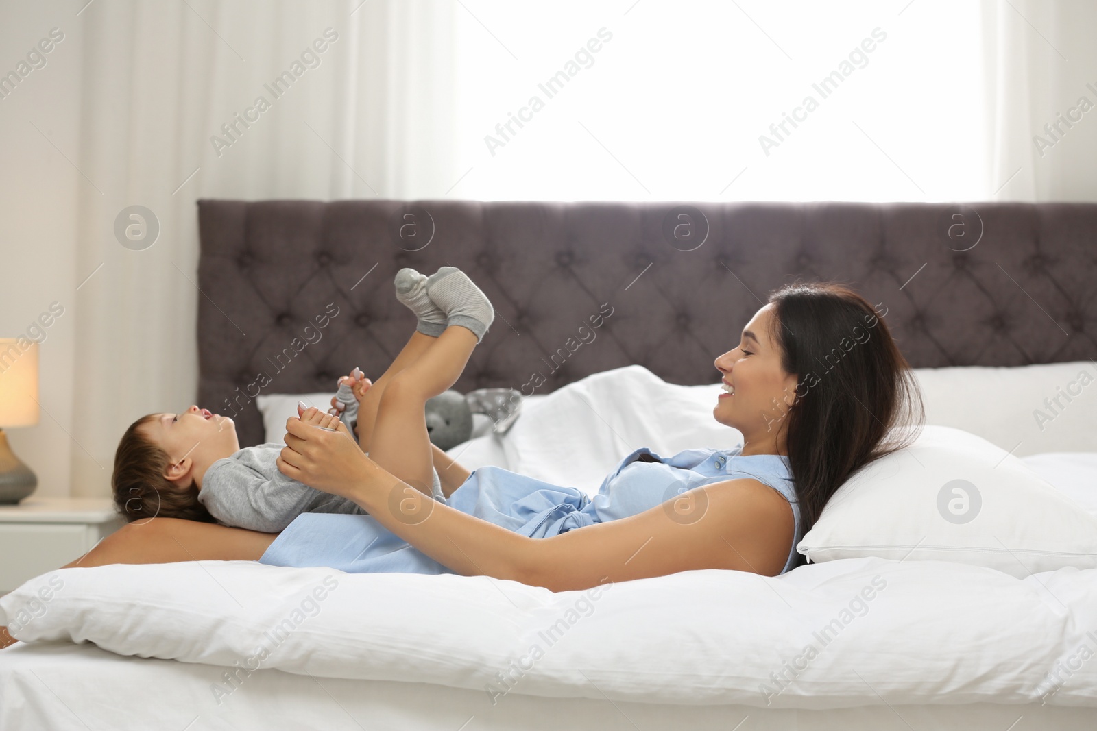 Photo of Young nanny playing with cute little baby in bedroom