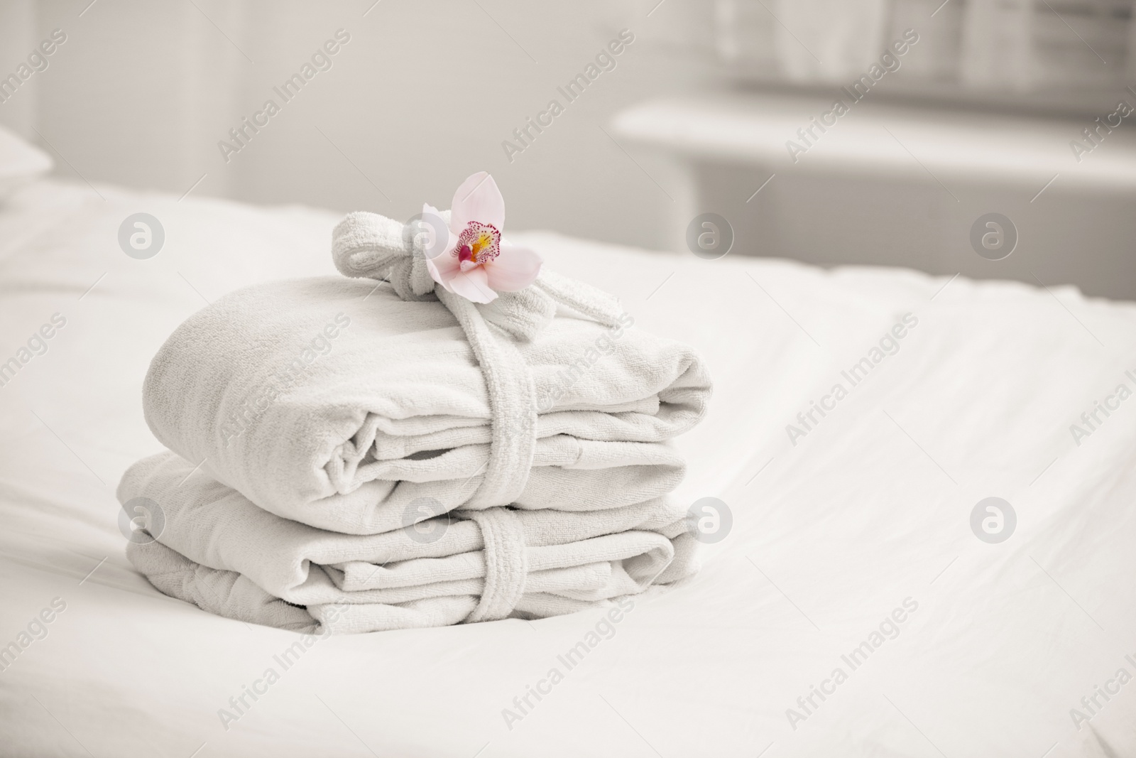 Photo of Clean folded bathrobes on bed in room, space for text