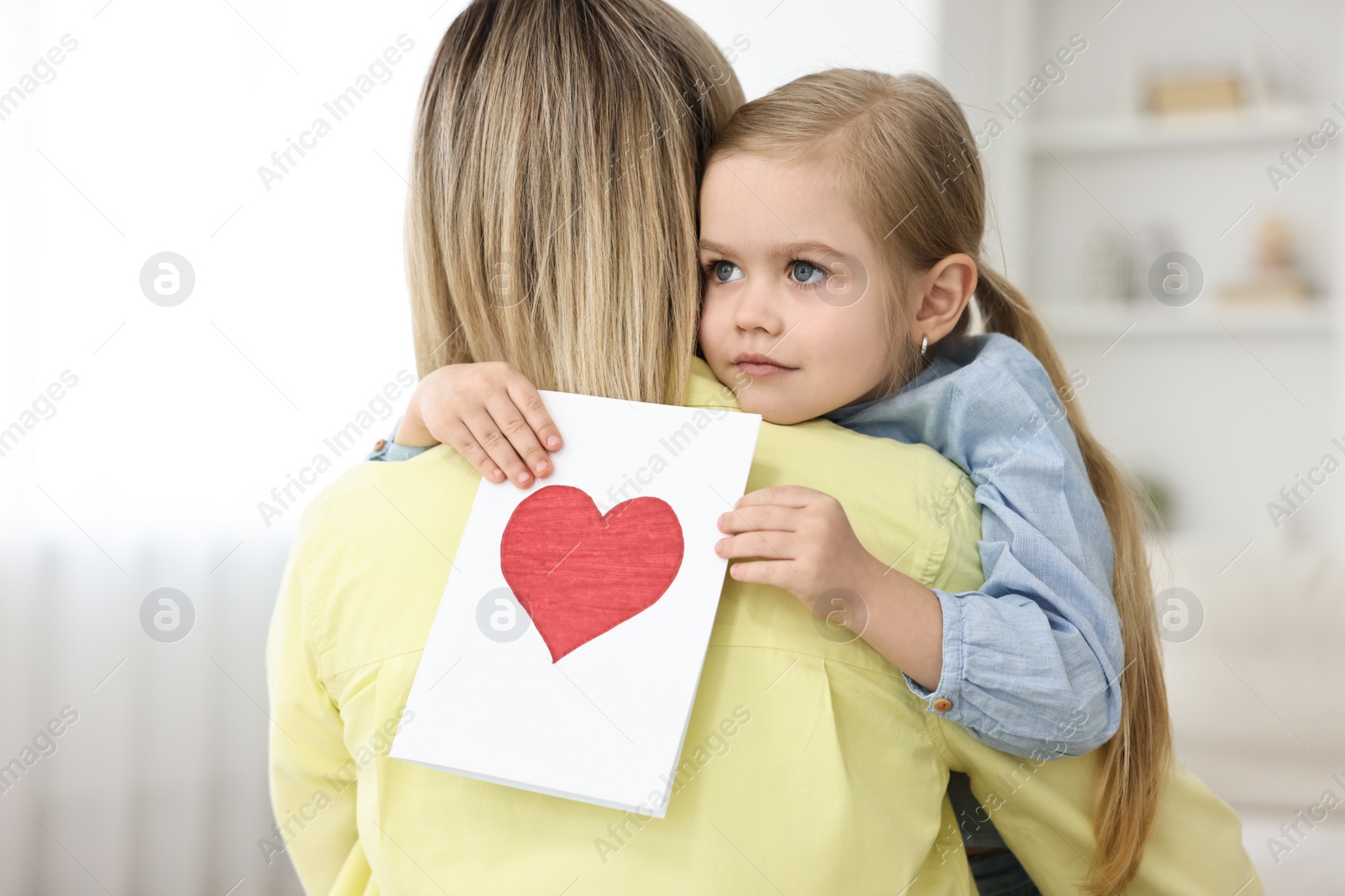 Photo of Little daughter congratulating her mom with greeting card at home. Happy Mother's Day