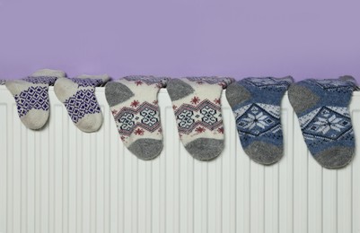 Knitted socks on heating radiator near violet wall