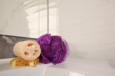 Photo of Purple shower puff, loofah sponge and soap on sink in bathroom, space for text