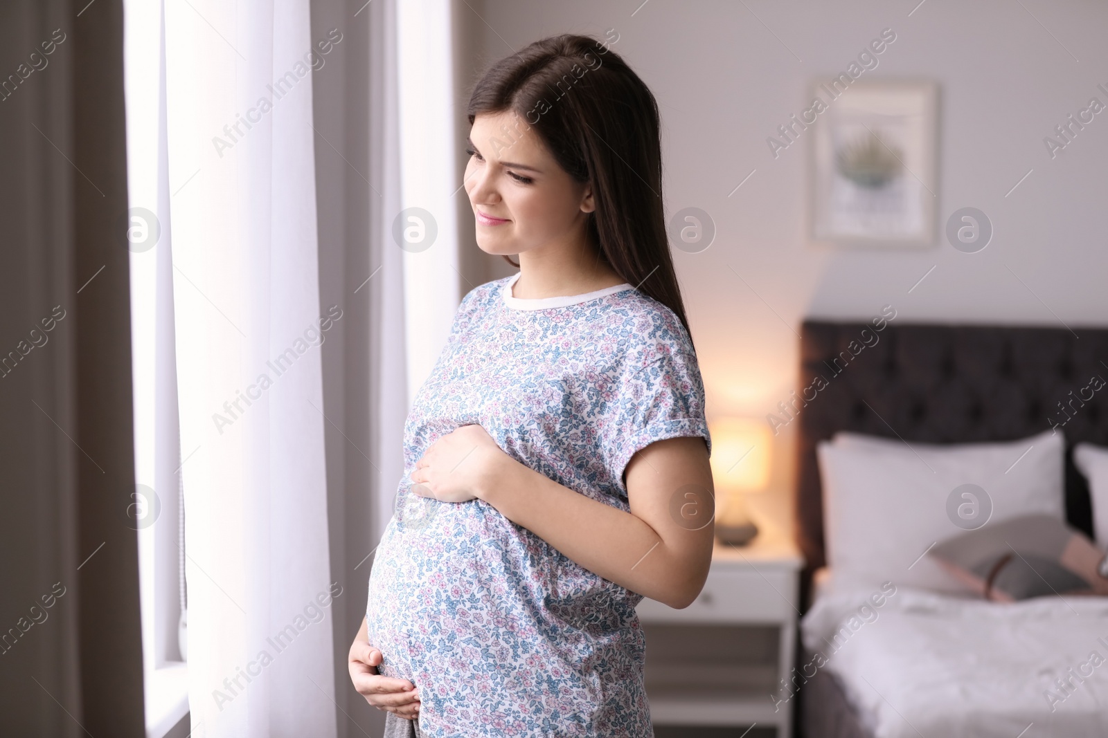 Photo of Young pregnant woman near window at home