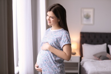 Young pregnant woman near window at home