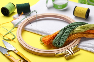 Embroidery hoop and different sewing accessories on yellow background