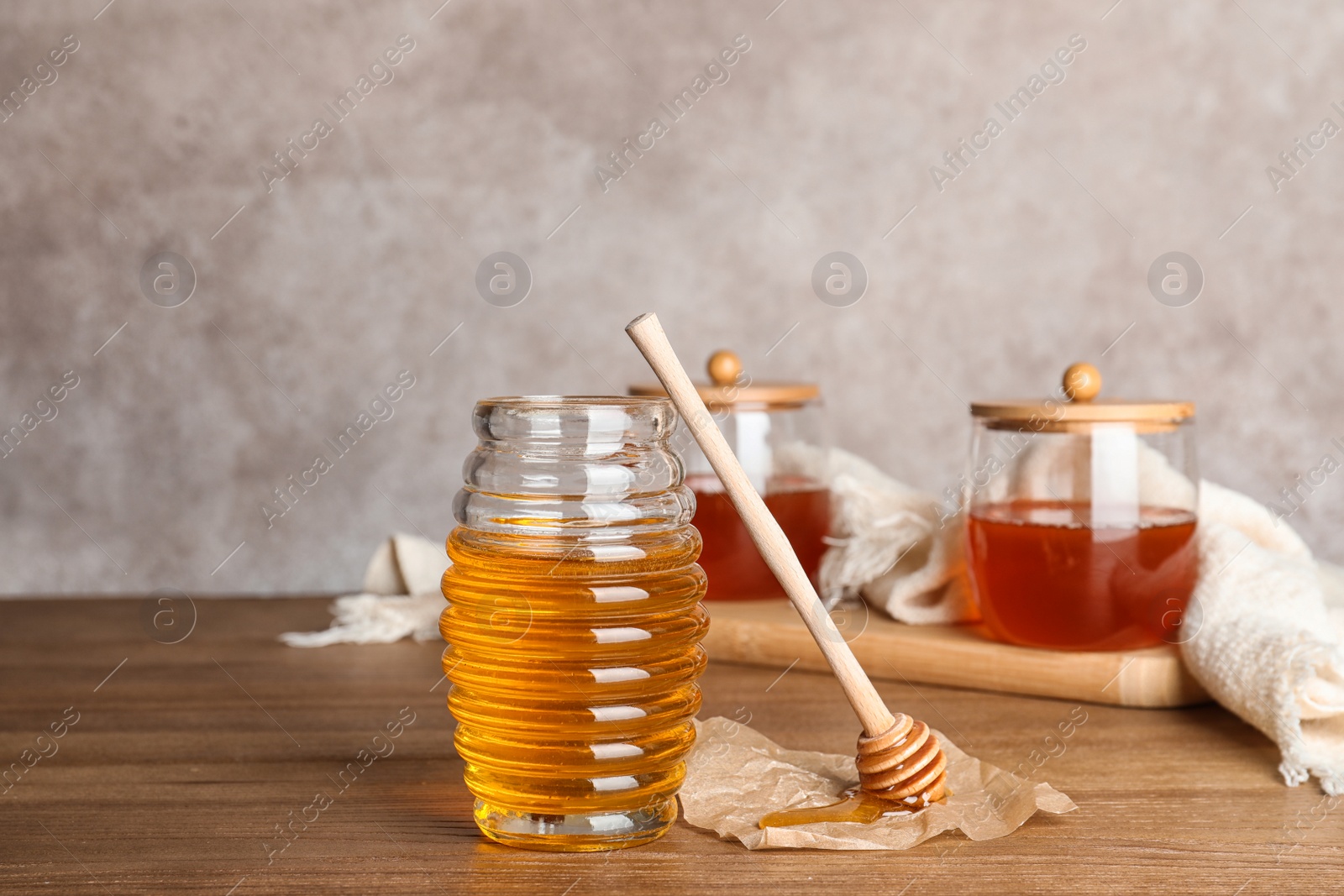 Photo of Glass jar with tasty honey and dipper on wooden table