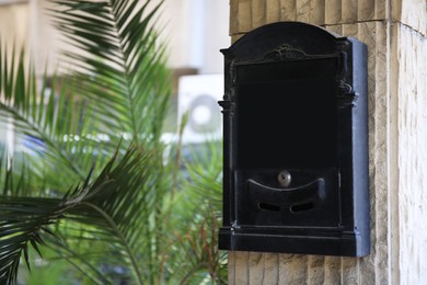 Photo of Black metal letter box on beige column outdoors, space for text