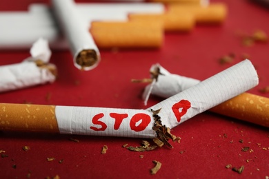 Photo of Broken cigarette with word Stop on red background, closeup. Quitting smoking concept