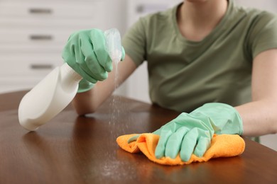 Photo of Woman with spray bottle and microfiber cloth cleaning wooden table in room, closeup