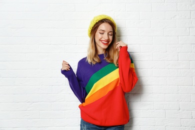 Beautiful young woman in warm sweater with hat near white brick wall