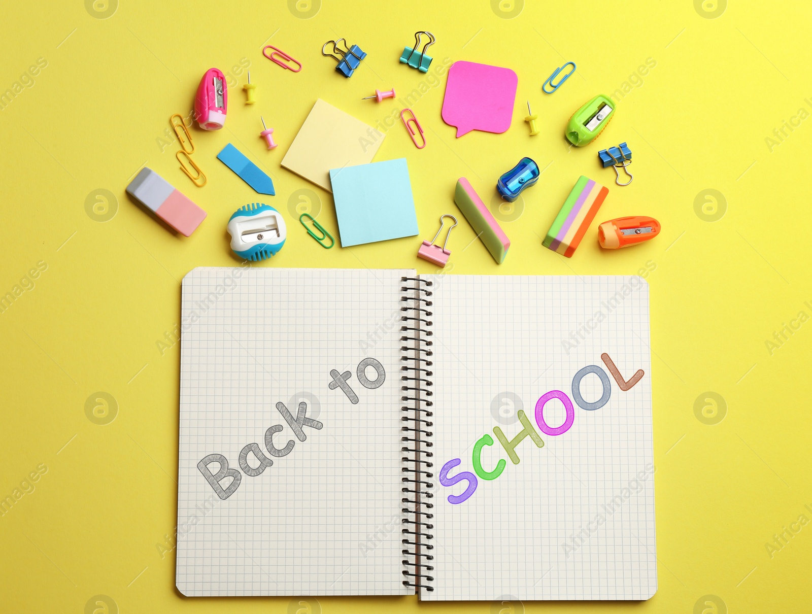 Image of Notebook with text Back To School near different stationery on yellow, flat lay