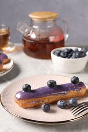 Photo of Tasty glazed eclair with blueberries on grey marble table, closeup