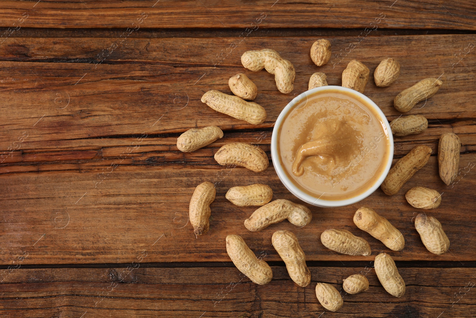 Photo of Delicious nut butter in bowl and peanuts on wooden table, top view. Space for text