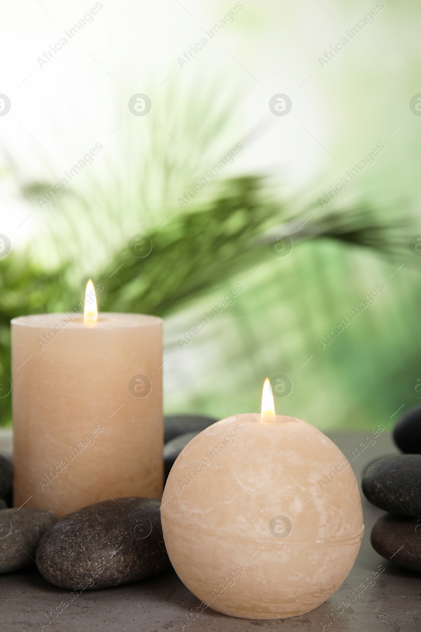 Photo of Burning candles and spa stones on table against blurred green background, space for text