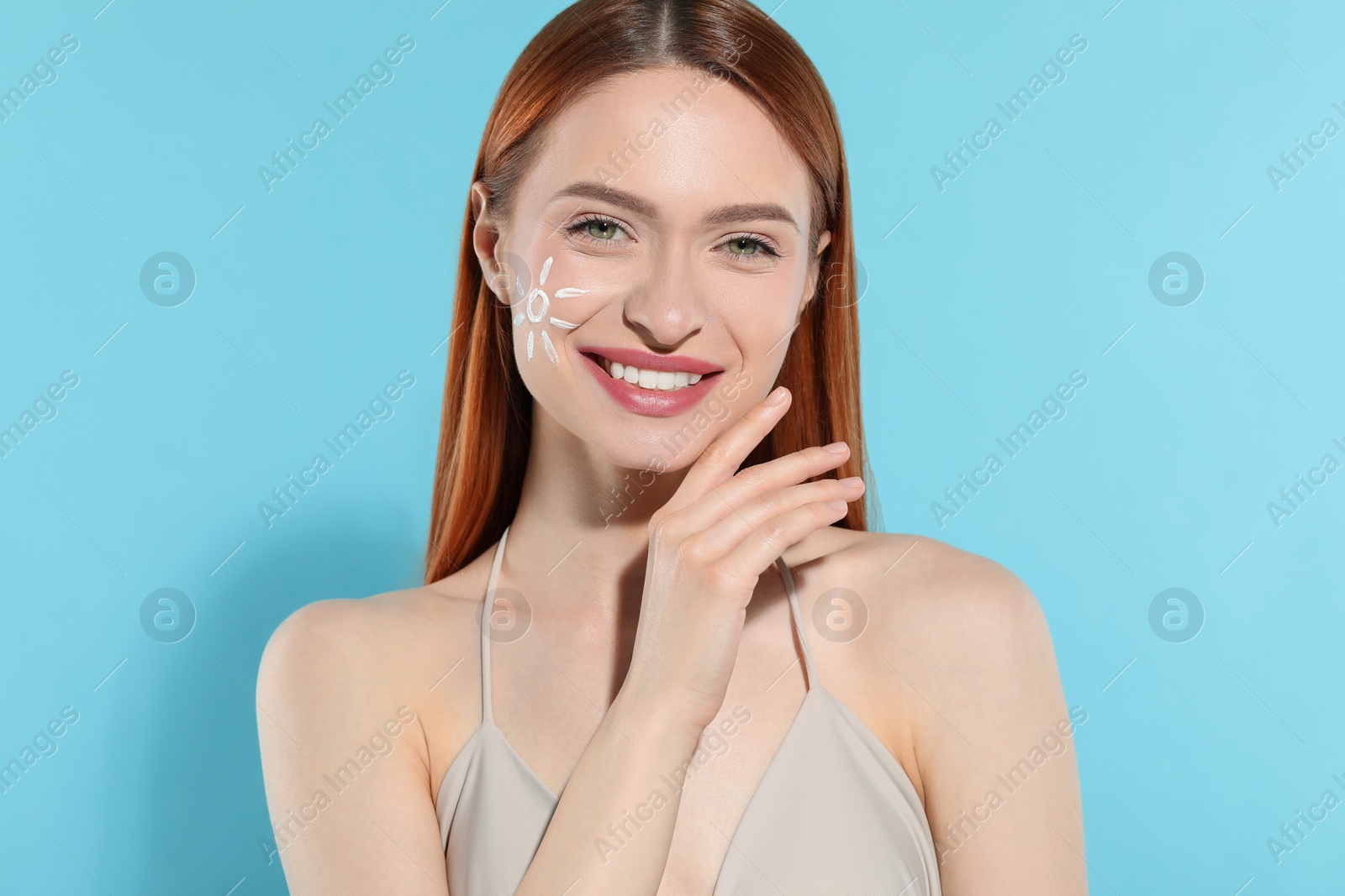 Photo of Beautiful young woman with sun protection cream on her face against light blue background