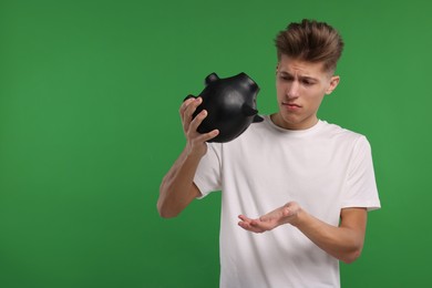 Photo of Upset man with empty piggy bank on green background. Space for text