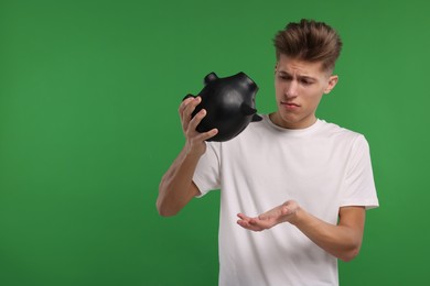 Upset man with empty piggy bank on green background. Space for text