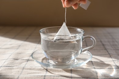 Photo of Woman dipping tea bag into cup with water at table, closeup