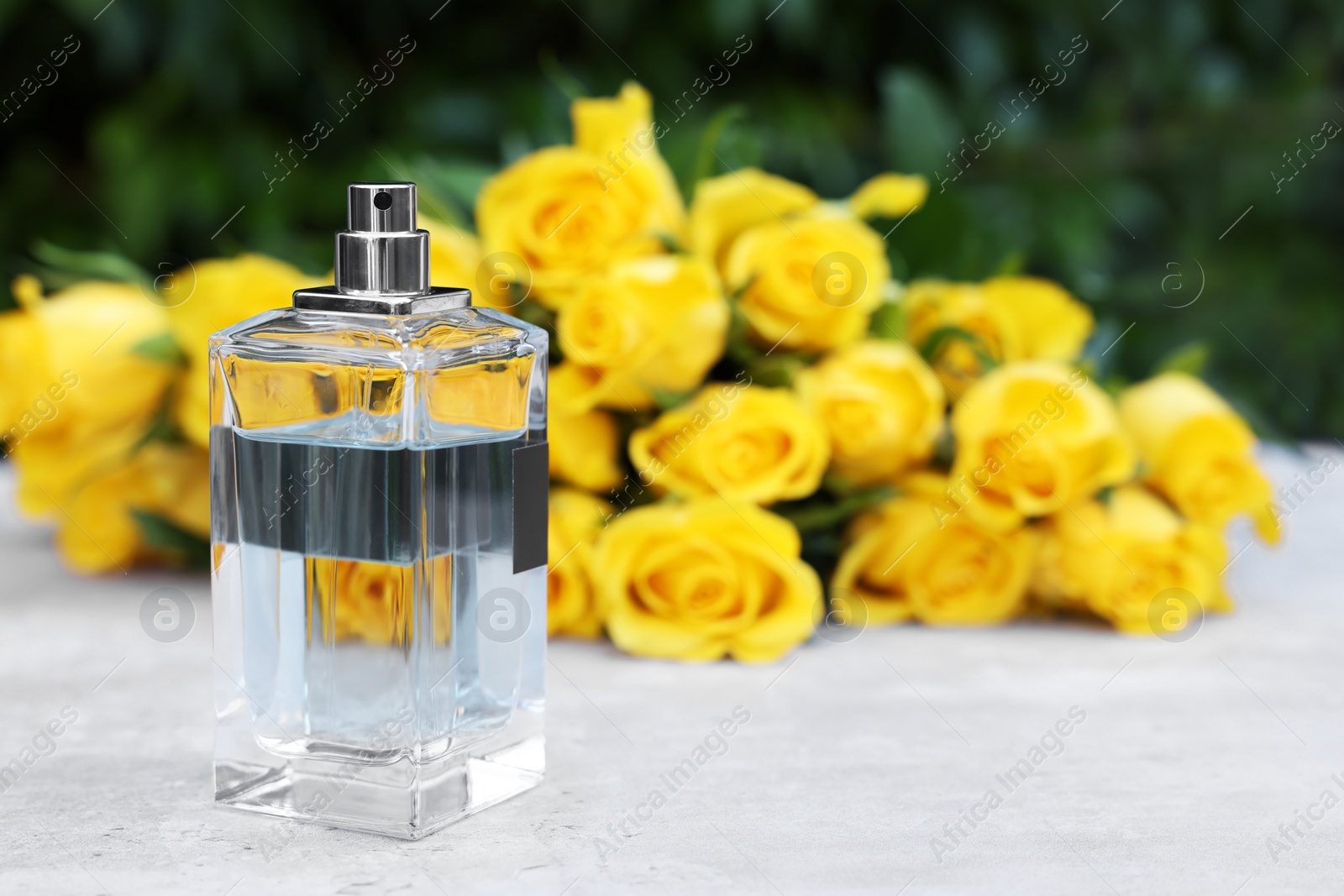 Photo of Perfume and beautiful bouquet of yellow roses on light table outdoors, selective focus. Space for text