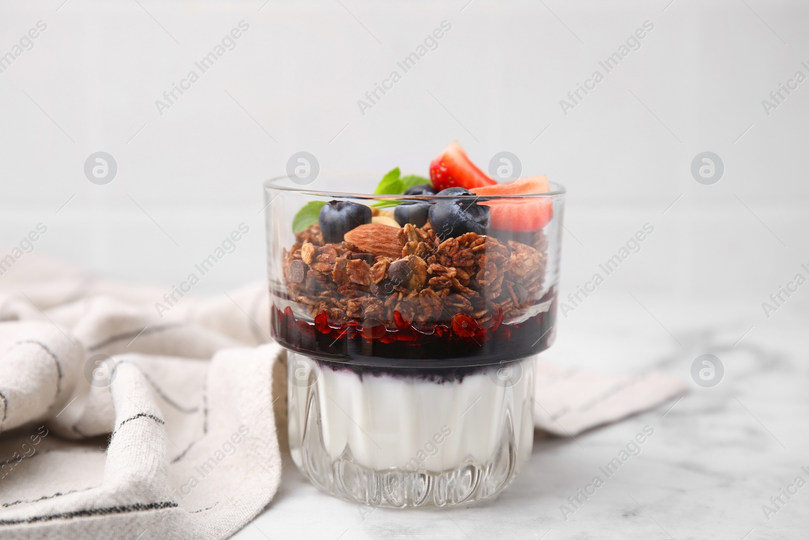 Photo of Tasty granola with berries, jam and yogurt in glass on white marble table