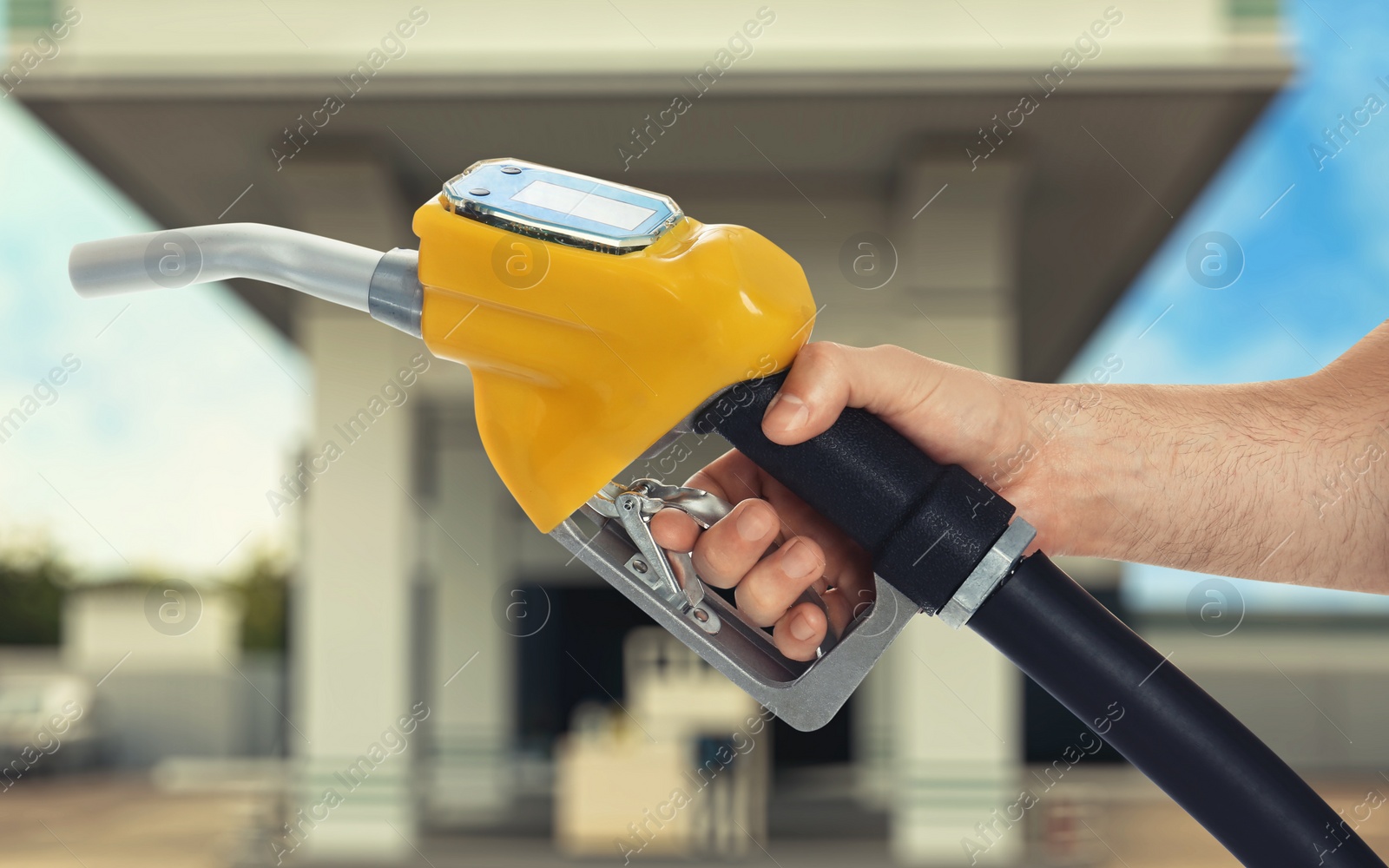 Image of Man holding fuel nozzle near gas station, closeup