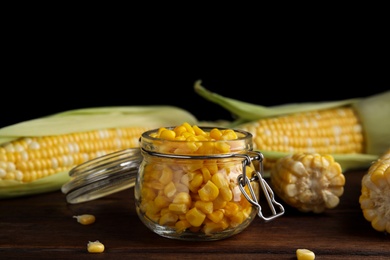 Photo of Tasty sweet corn kernels in jar and fresh cobs on wooden table