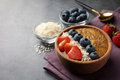 Photo of Delicious smoothie bowl with fresh berries, chia seeds and coconut flakes on grey table, closeup. Space for text